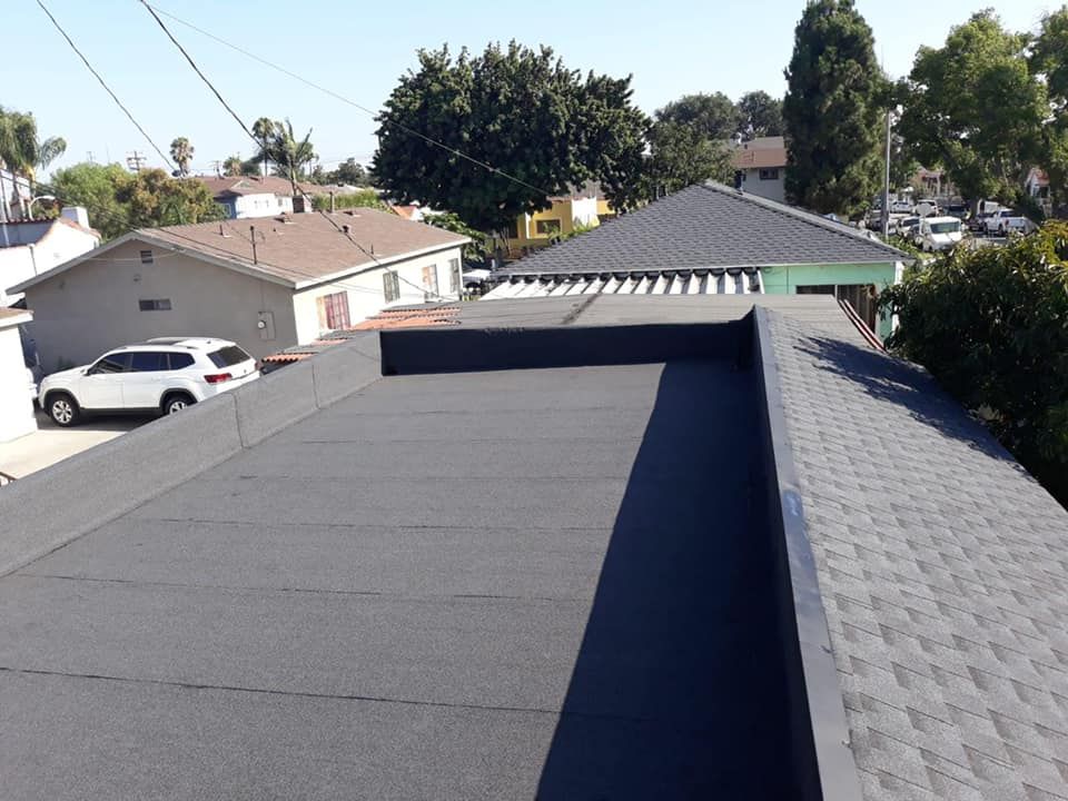 Black flat roof, gray shingled roof, houses, blue sky, and a white car in the background.