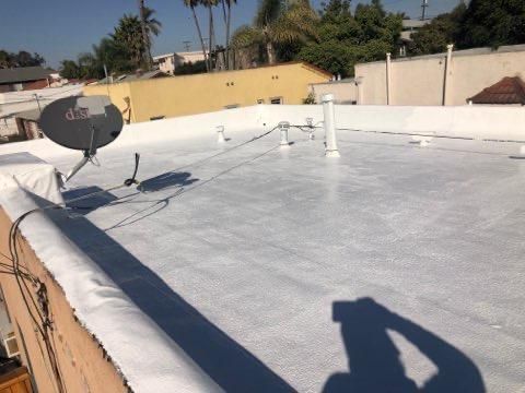 White-coated flat roof with satellite dish, pipes, and wires against a sunny backdrop.