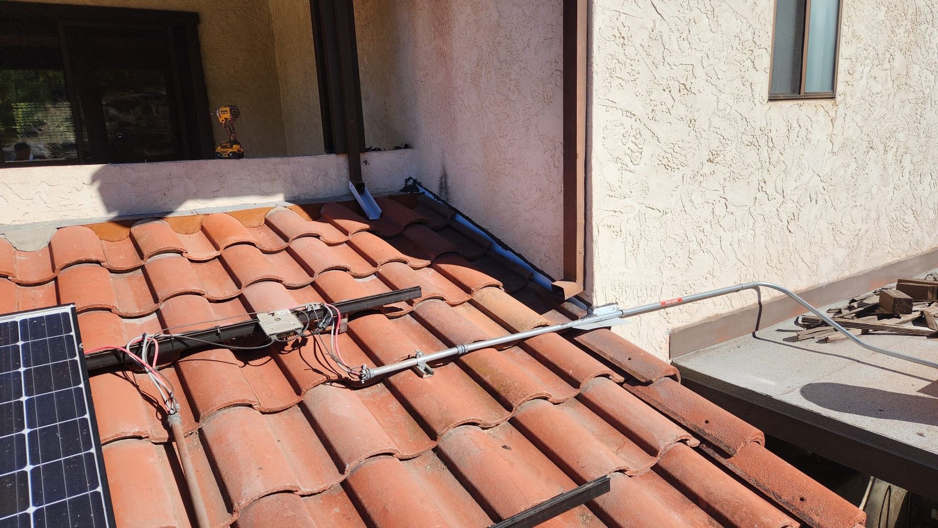 Solar panels on a terracotta tile roof, with cabling and a gutter in the background, near a stucco wall.