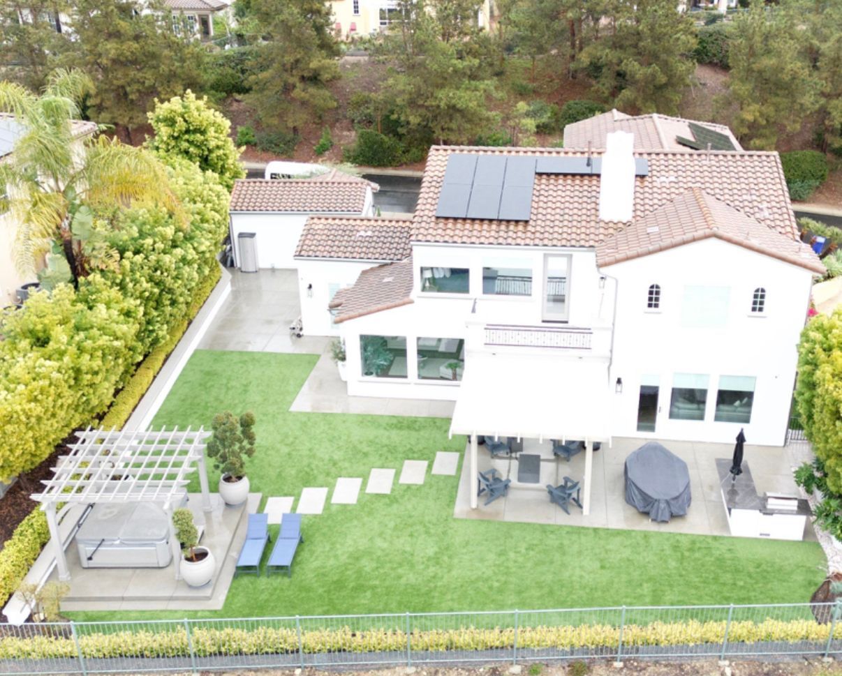 Aerial view of a white house with solar panels, a green lawn, and patio seating.