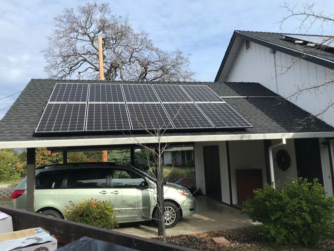 Solar panels on a carport roof above a parked green minivan. Sunny day, residential setting.