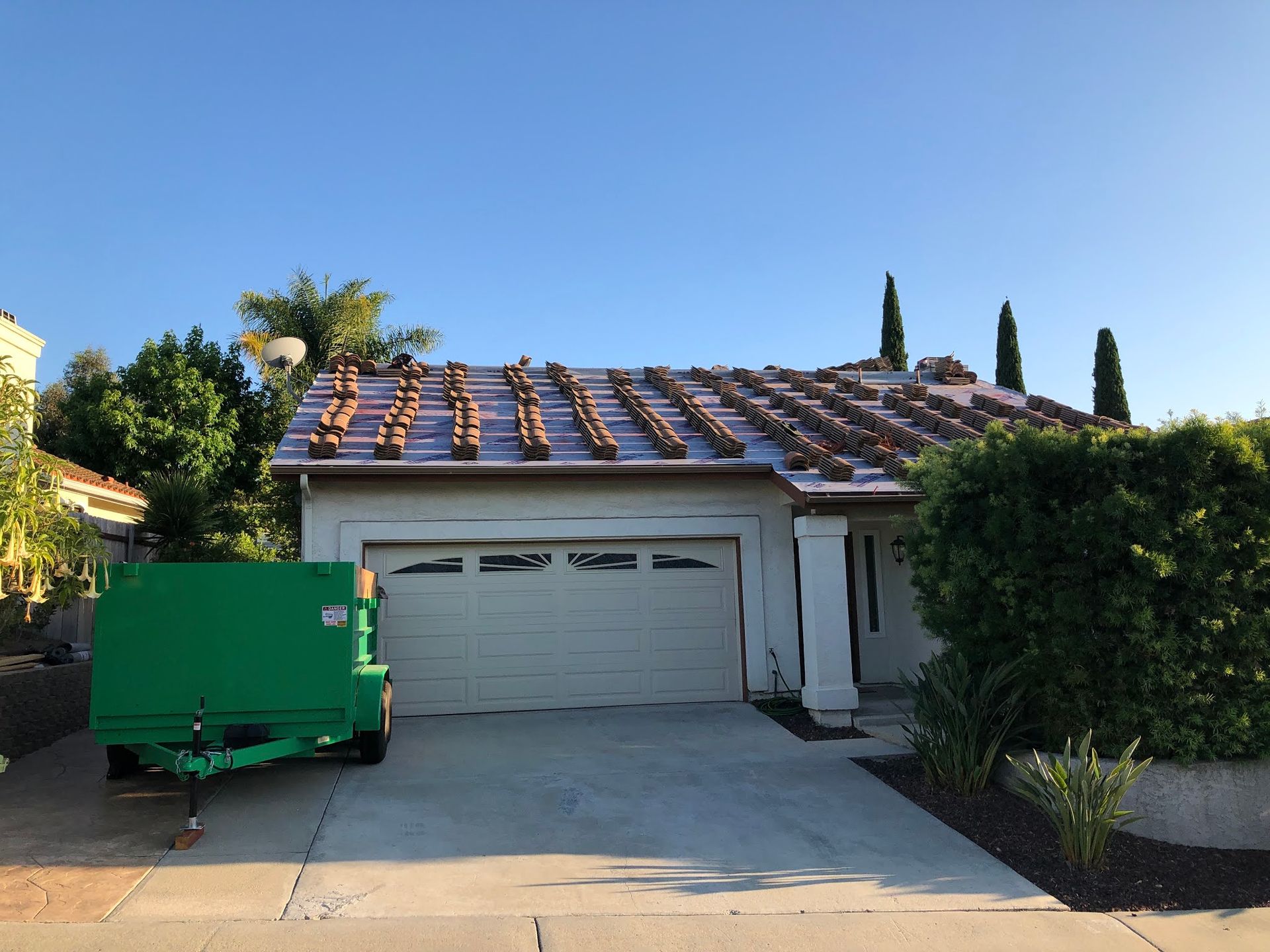 House with roof partially covered with brown tiles, a green dumpster, and a driveway.