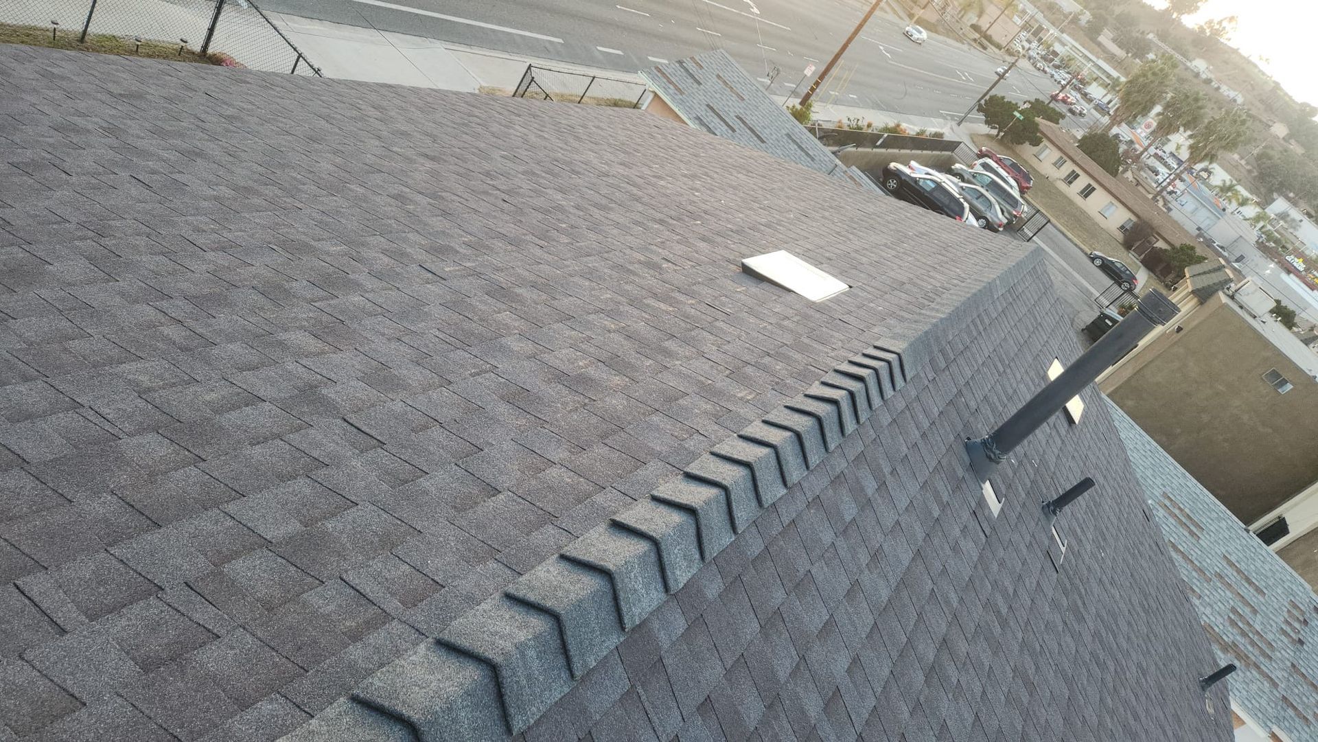 Gray shingle roof of a building with a vent and flashing detail; outdoors.