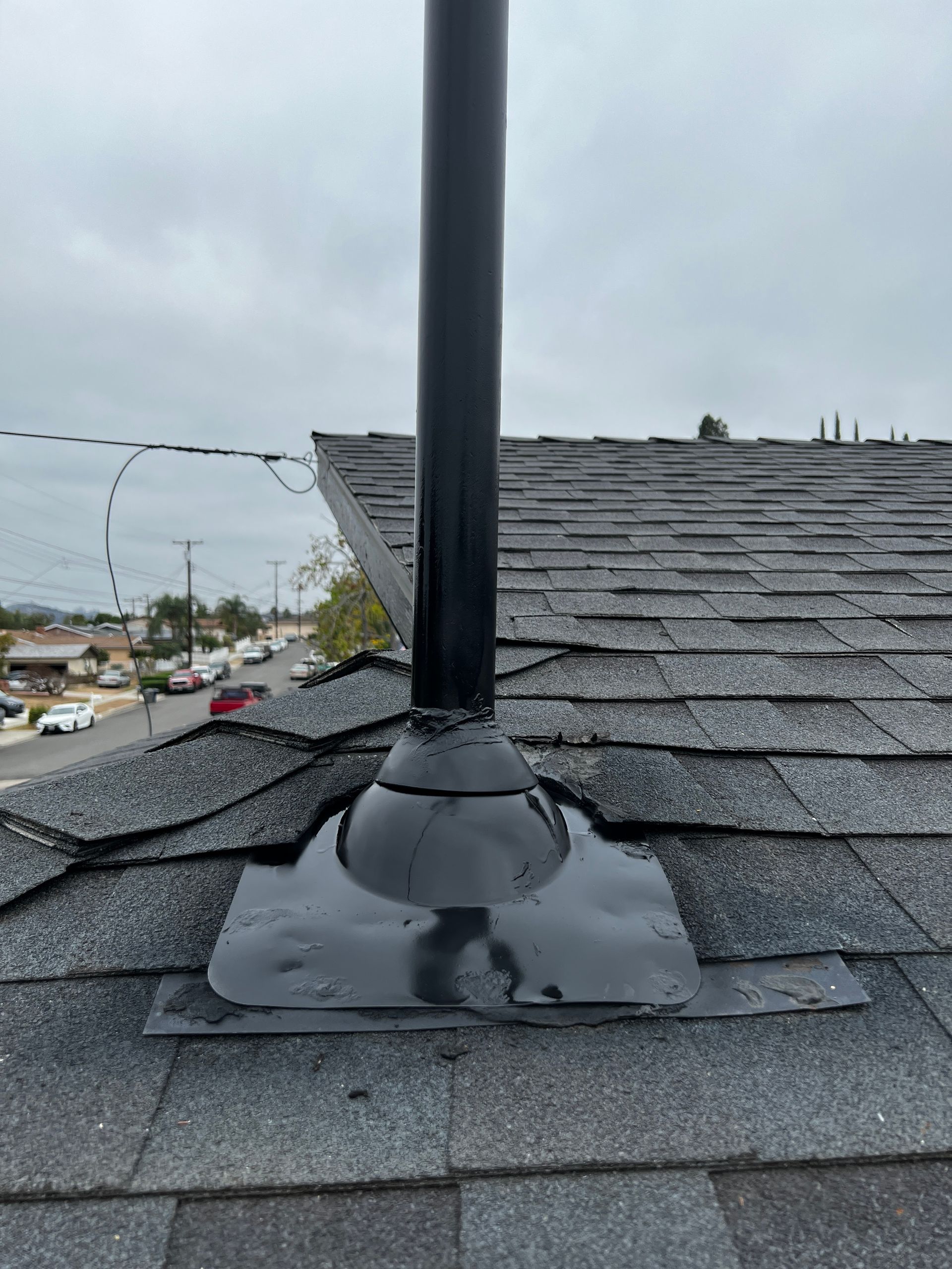Black chimney pipe on a shingled roof, with flashing. Cloudy sky in background.