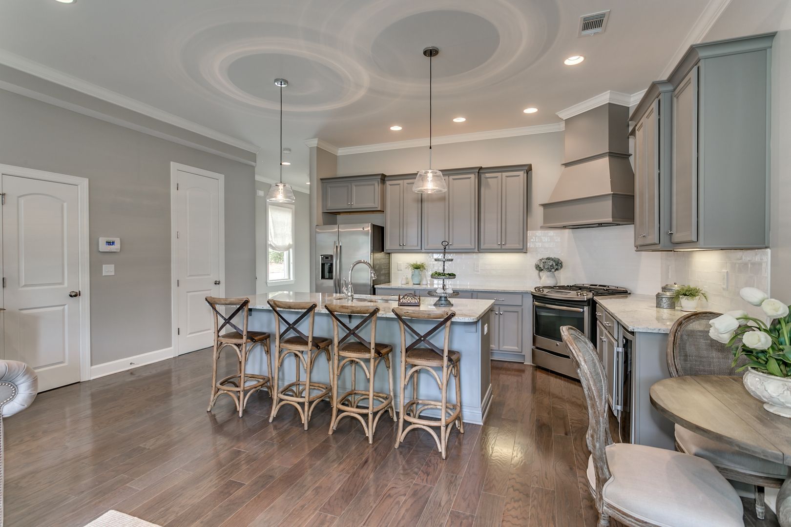 Kitchen with gray cabinets, island seating, wood floor, and overhead lighting.