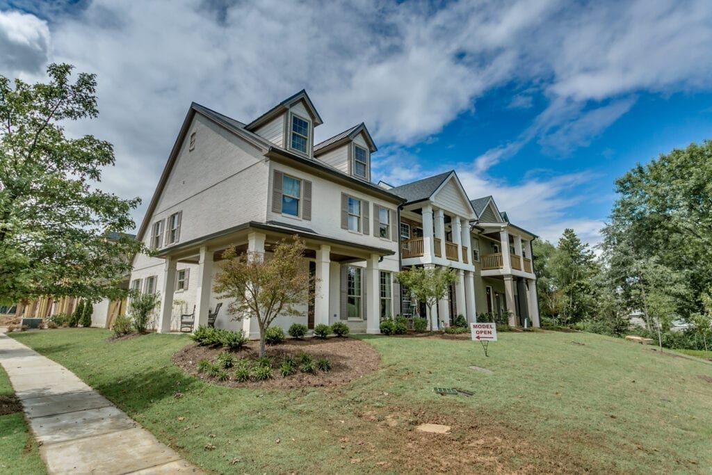 Two-story stucco house with a manicured lawn, blue sky, and trees.