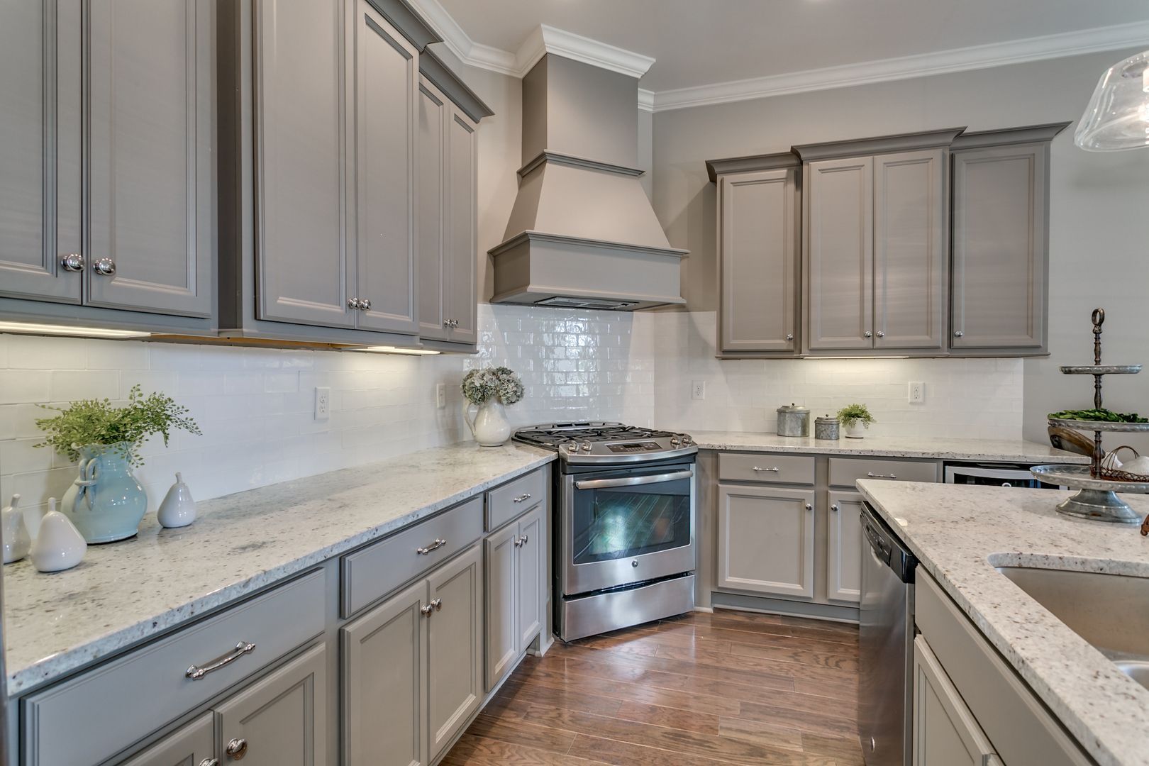 Gray kitchen cabinets with white countertops, stainless steel appliances, and tile backsplash.