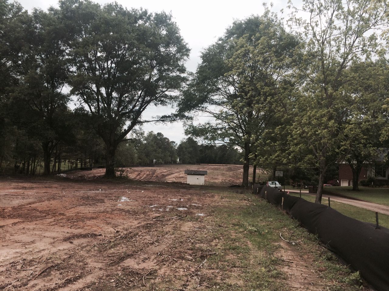 Cleared land with dirt and trees in the background, a small white structure in the middle.