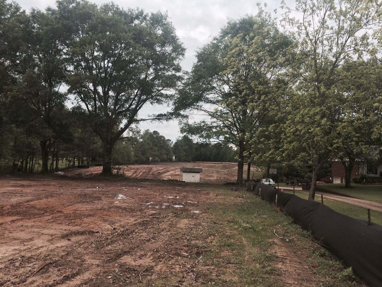 Cleared land with trees in the background, a small white structure, and a silt fence.