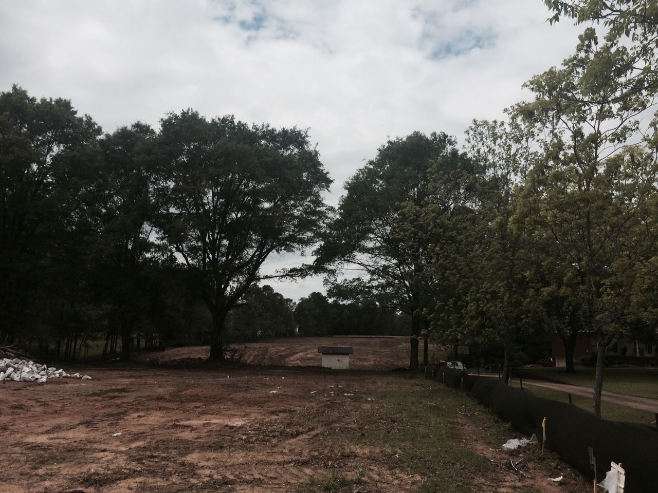 Open field with trees and cloudy sky. A small structure sits in the distance.