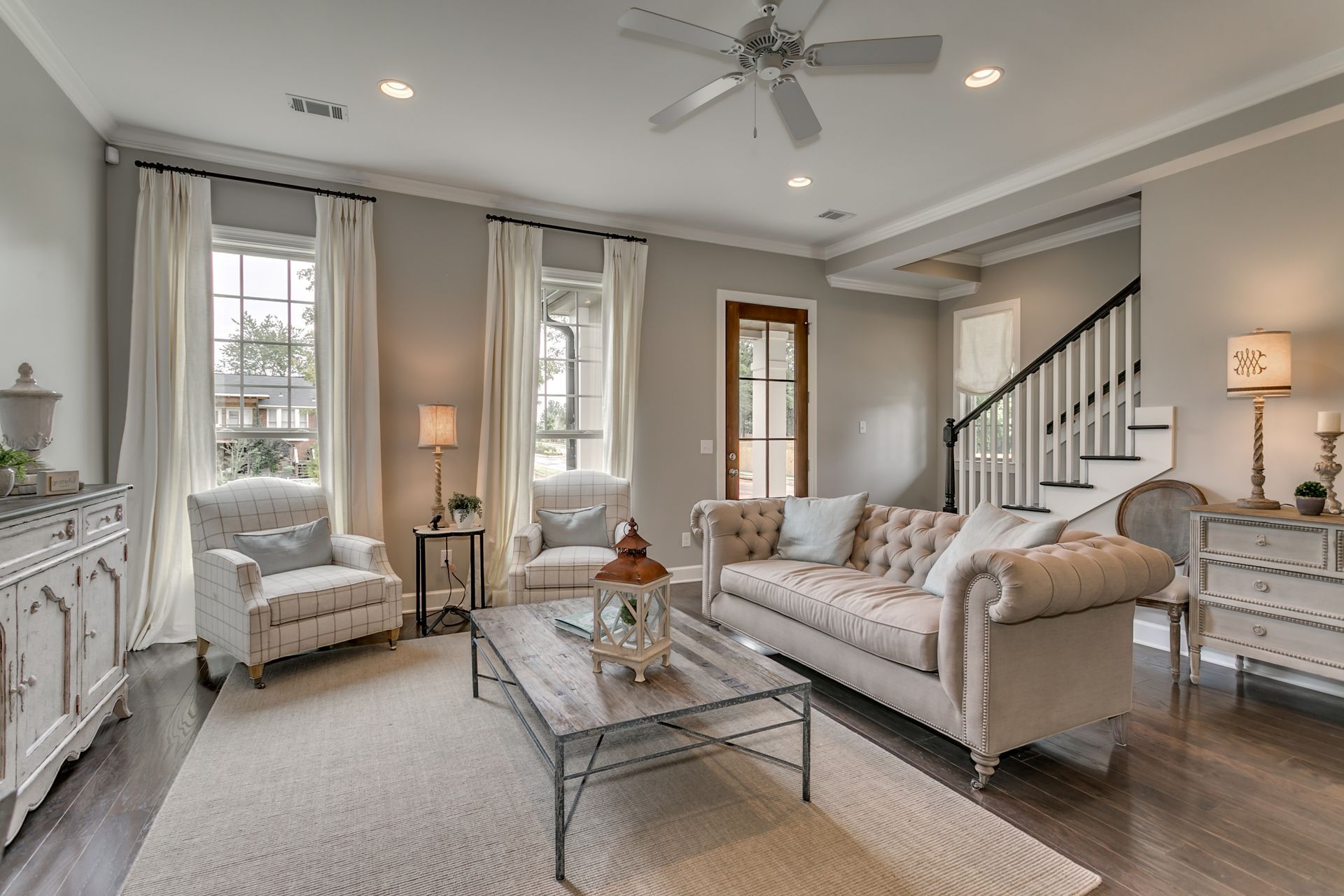 Living room with gray walls, white trim, tufted sofa, two armchairs, and a rug.