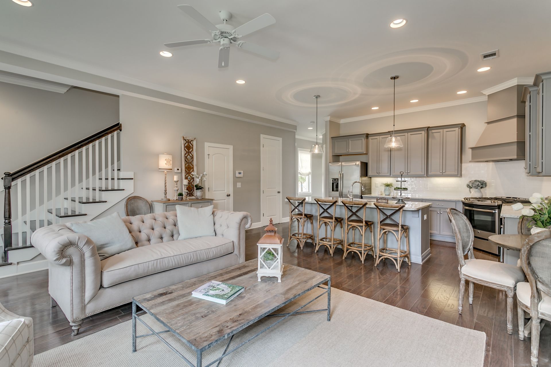 Open-concept living room and kitchen; gray walls, tufted sofa, island with seating, dark wood floors.