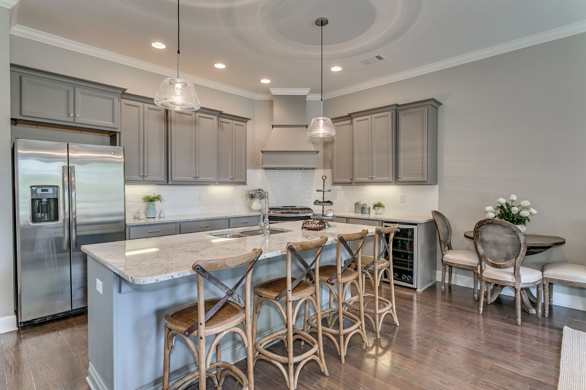 Gray kitchen with island seating, stainless steel fridge, and small round table.