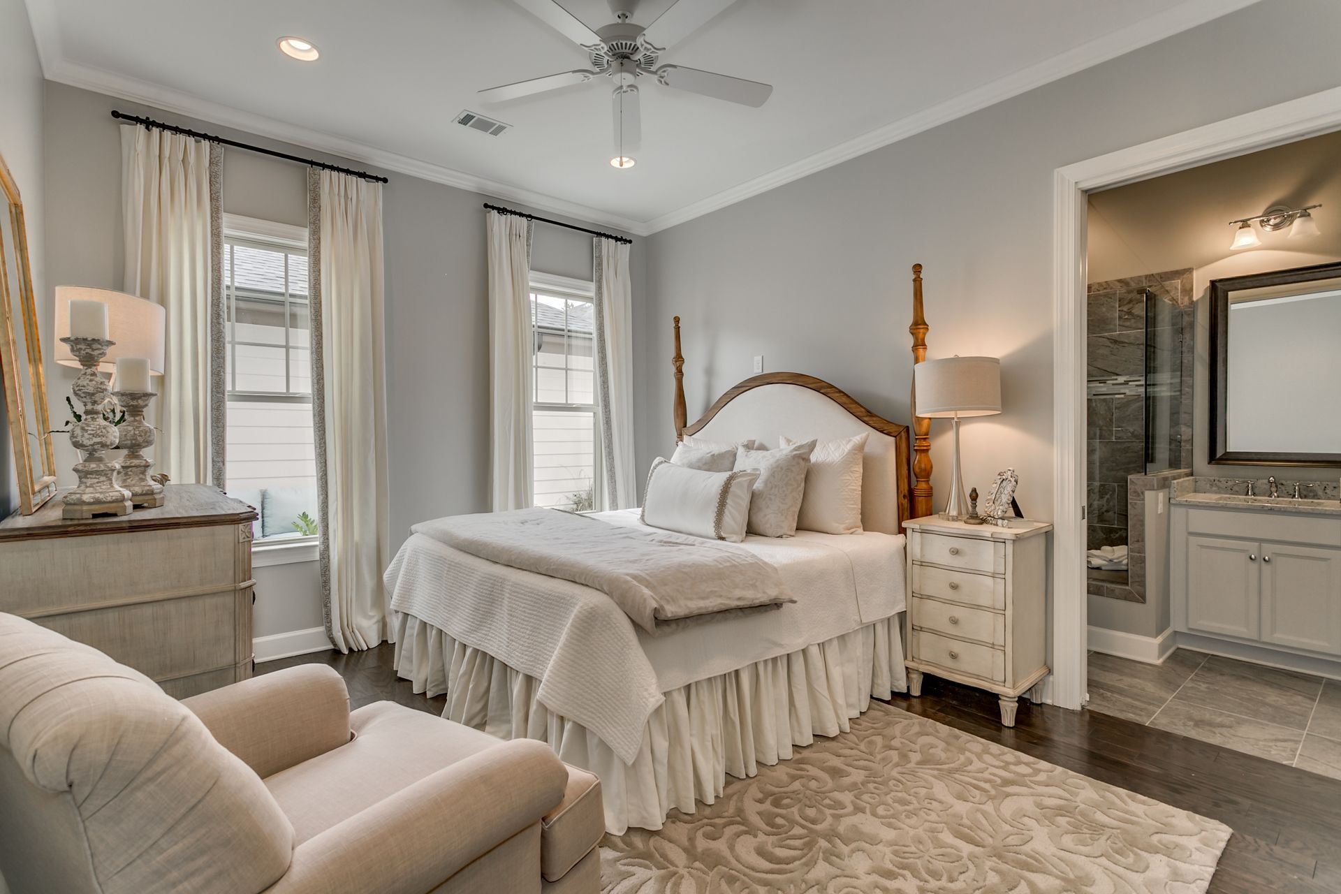 Bedroom with a four-poster bed, windows, cream-colored furniture, and an open doorway to a bathroom.