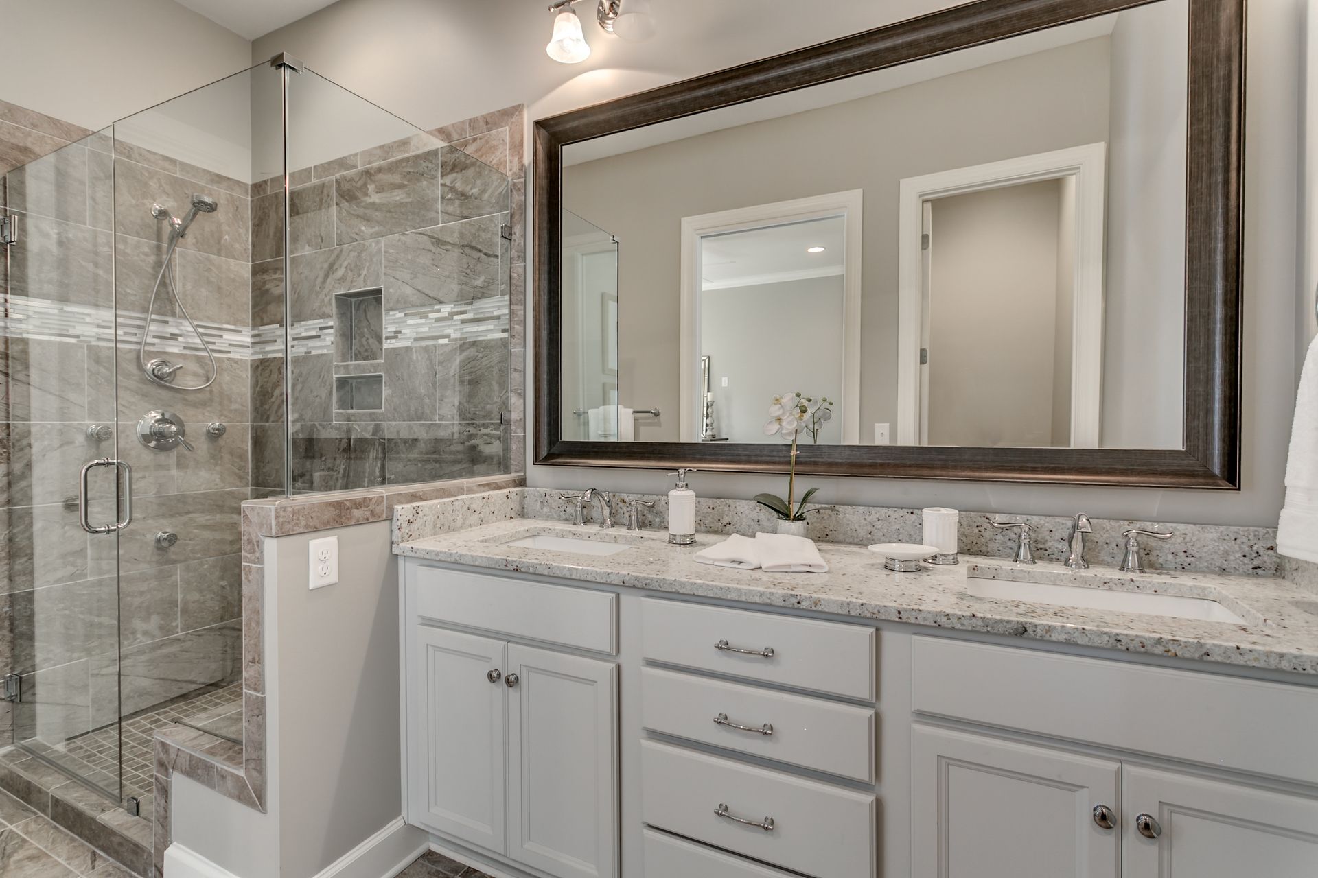Bathroom with a gray and white color scheme. It features a shower, a double vanity with a large mirror.