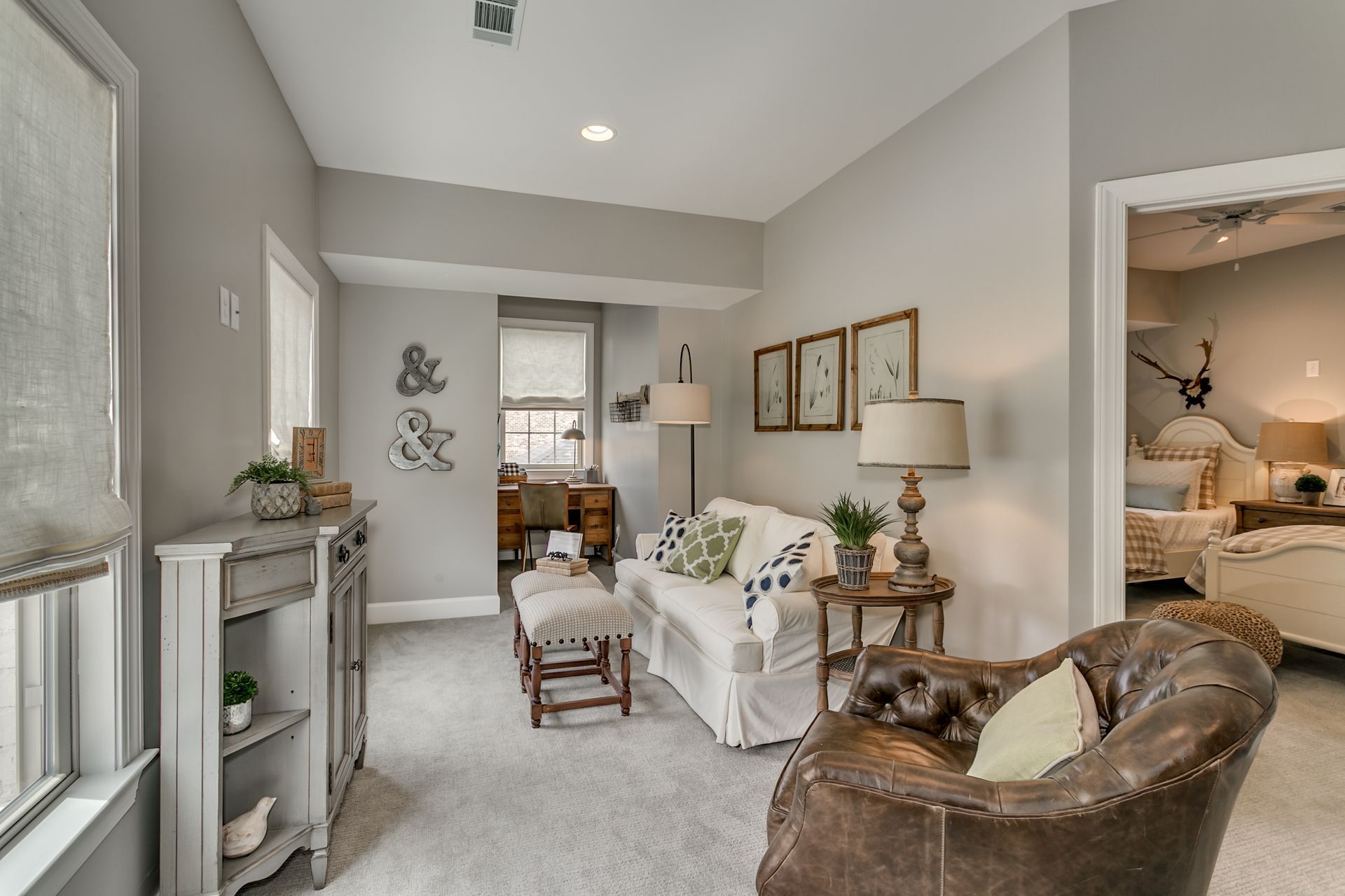 Cozy living room with gray walls, sofa, leather armchair, small table, and open doorway to a bedroom.