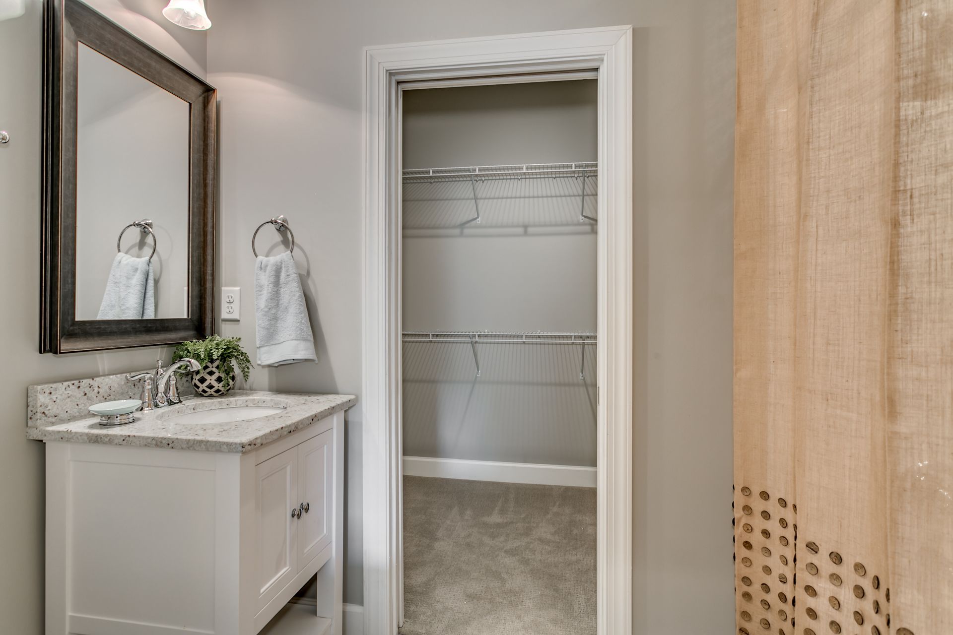 Bathroom with white vanity, large mirror, open closet, and tan shower curtain.