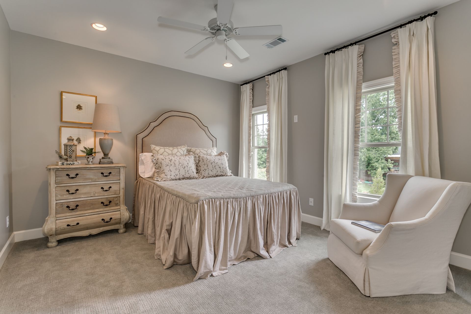 Bedroom with bed, dresser, chair, windows, and neutral color scheme.