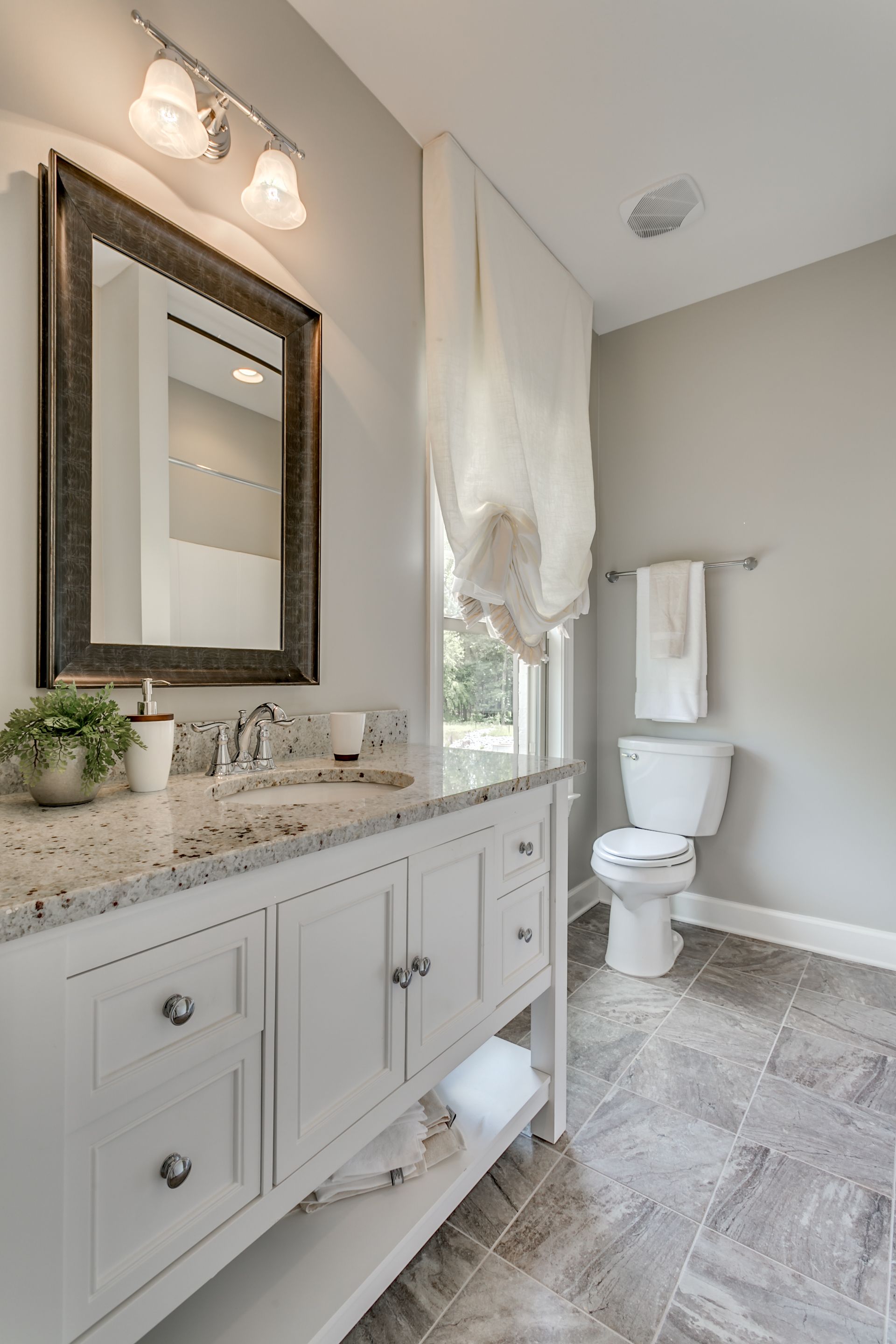 Bathroom with white vanity, gray walls, toilet, window, and gray tiled floor.