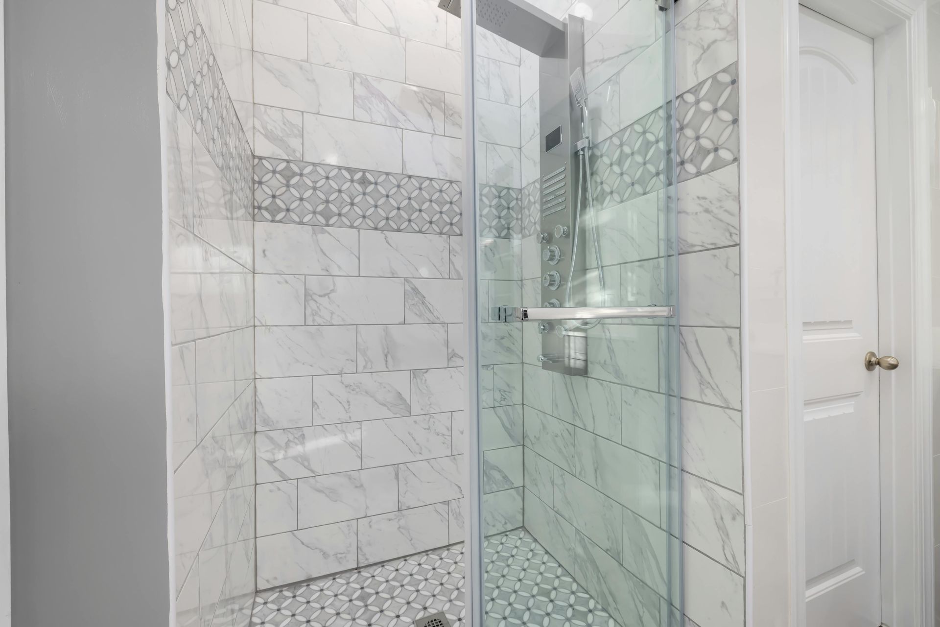 Shower with white marble tile and glass door, next to a white door.