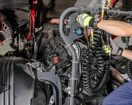 Person in gloves working on a truck engine with tools and hoses.