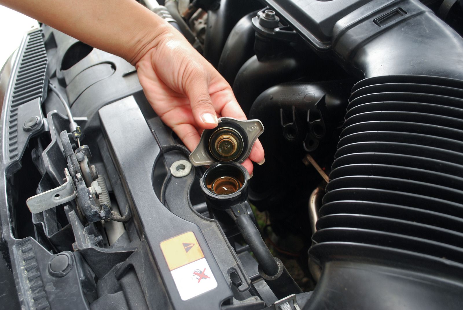 Hand opening radiator cap on a car engine, showing the coolant.