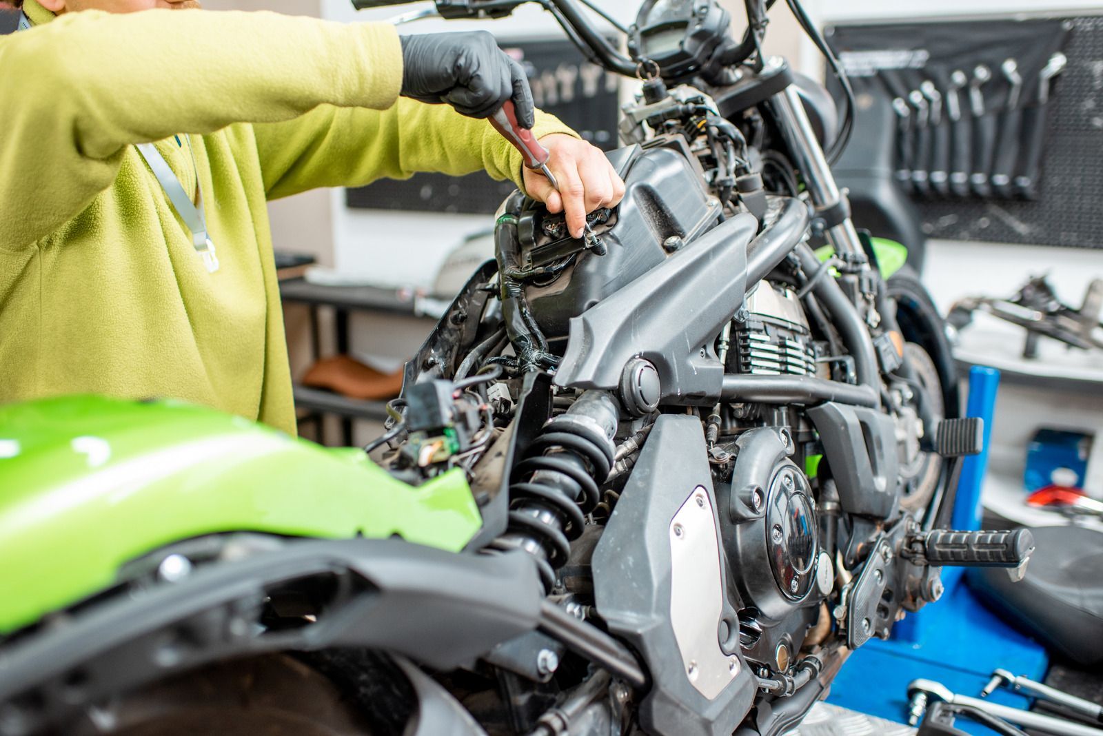 Person in green jacket working on a disassembled green and black motorcycle in a workshop.
