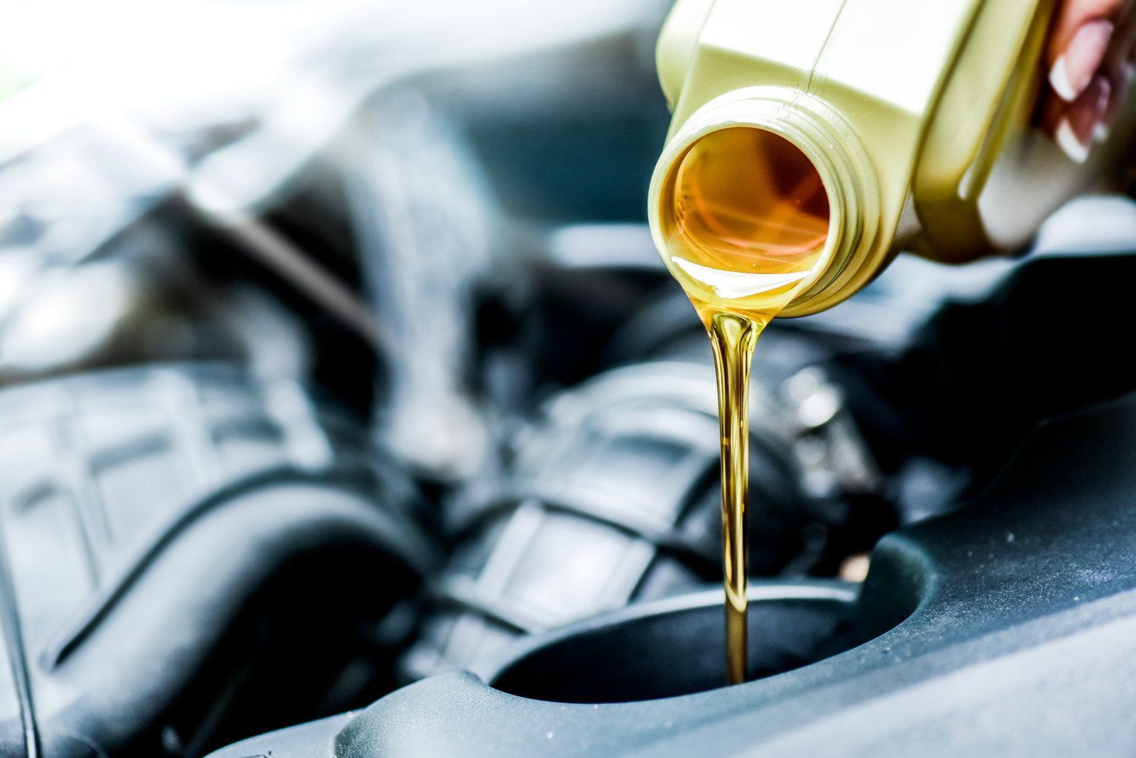 Pouring motor oil into a car engine; gold-colored liquid, dark engine bay, and yellow oil bottle.
