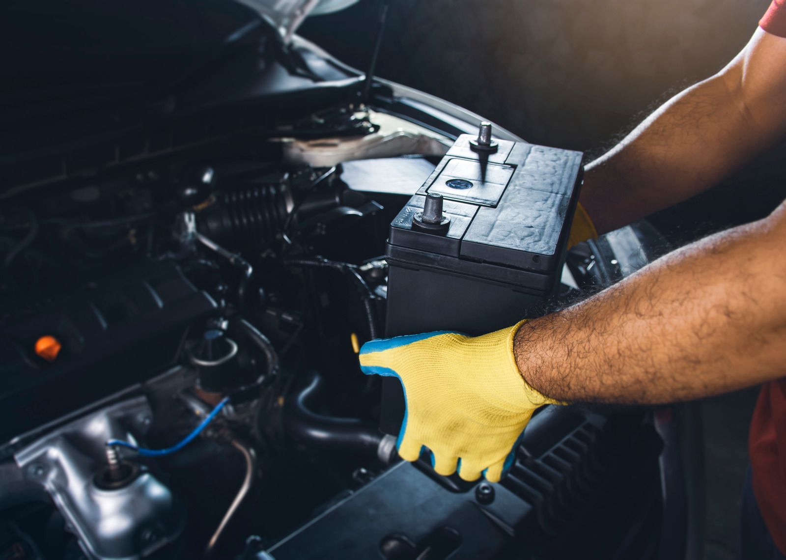 Person wearing gloves installing a car battery in an engine bay.