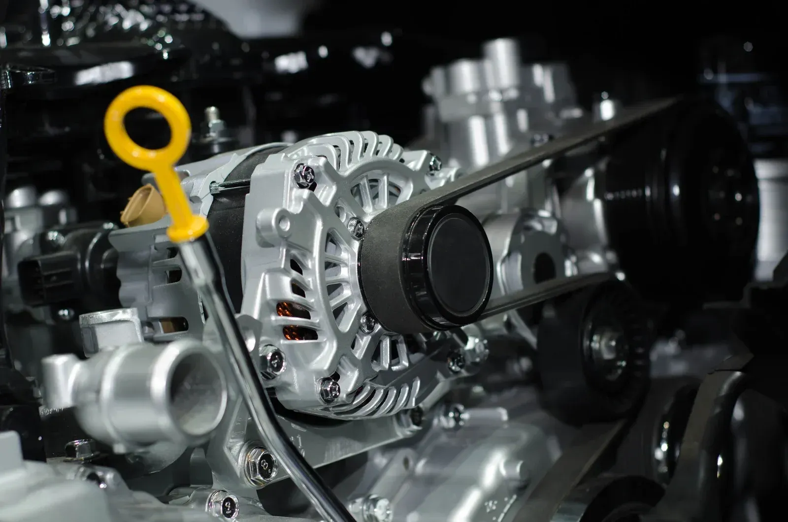 Close-up of a car engine with a silver alternator and a black belt.