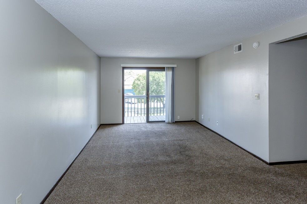 Empty room with light gray walls, brown carpet, and a sliding glass door to a balcony.