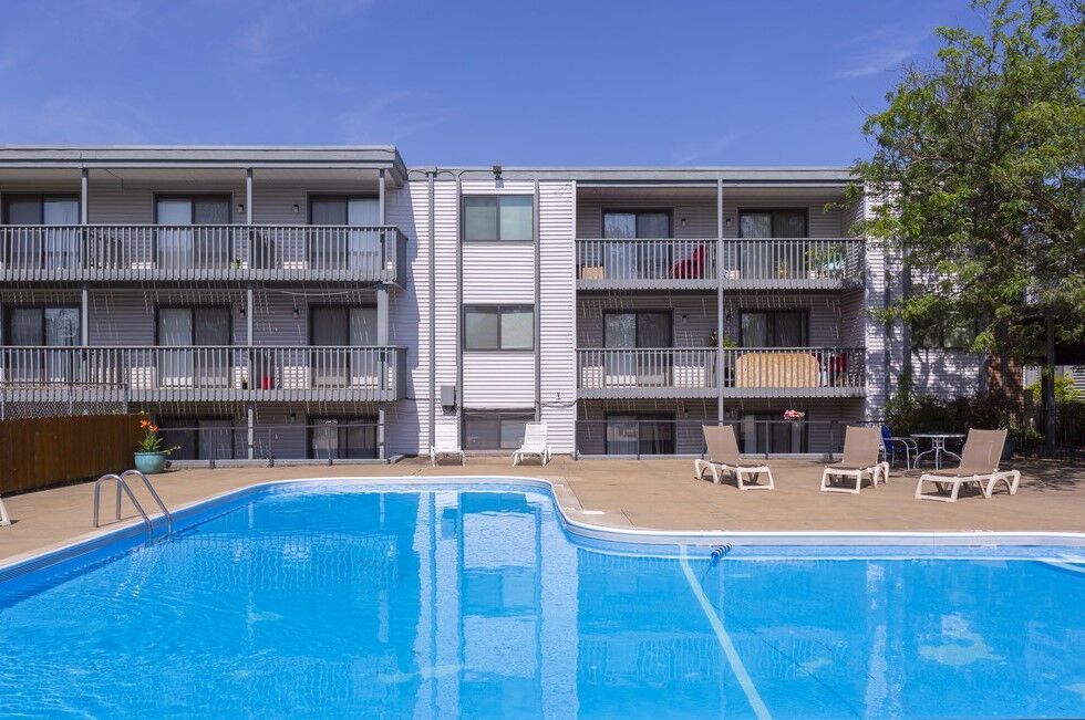 Apartment building with balconies and a pool on a sunny day. Loungers line the pool deck.