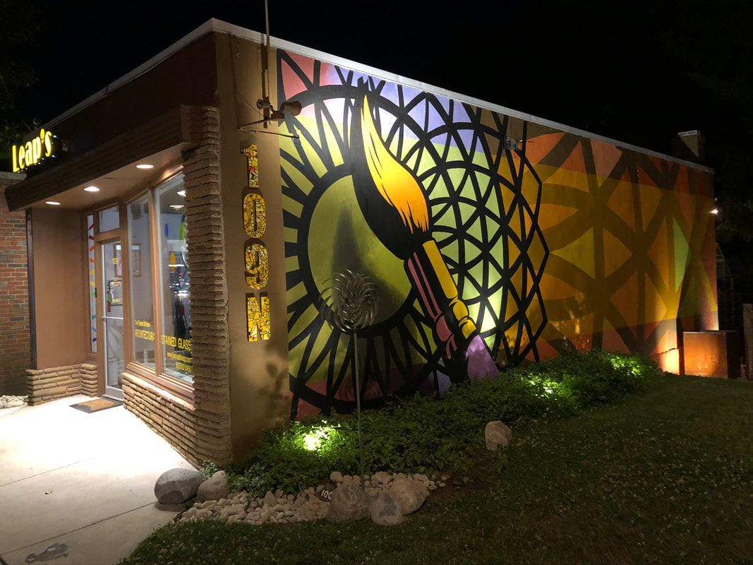 Nighttime view of a building with a colorful geometric mural and lit entrance walkway