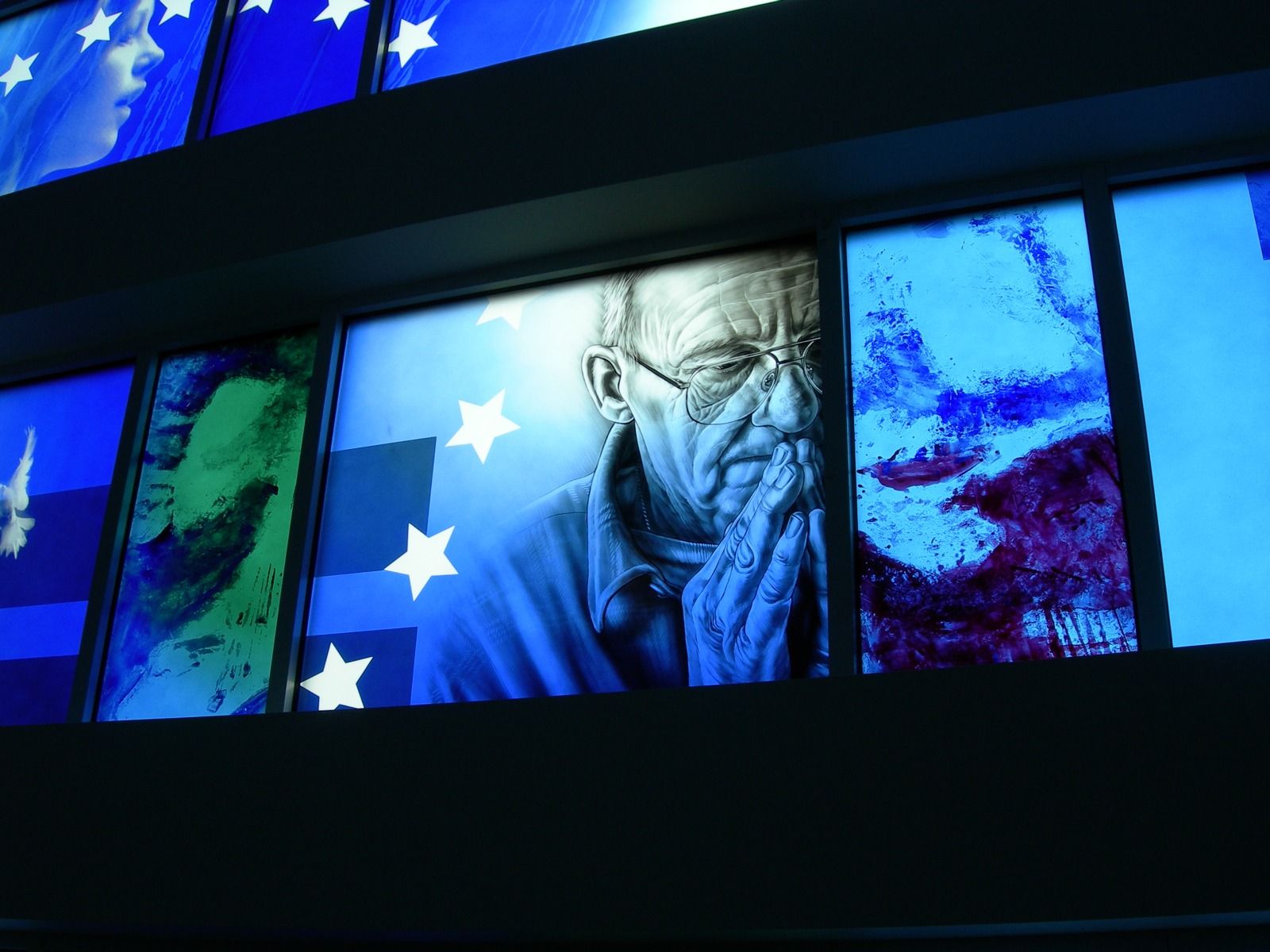 An illuminated panel display showing a person with glasses praying against a blue background with white stars.