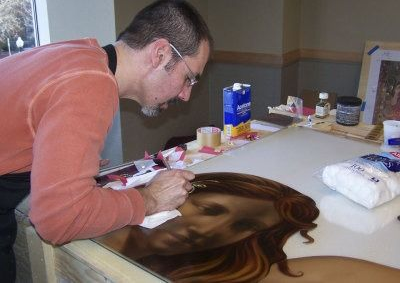 Man painting a woman’s portrait on a large canvas at a table with art supplies nearby