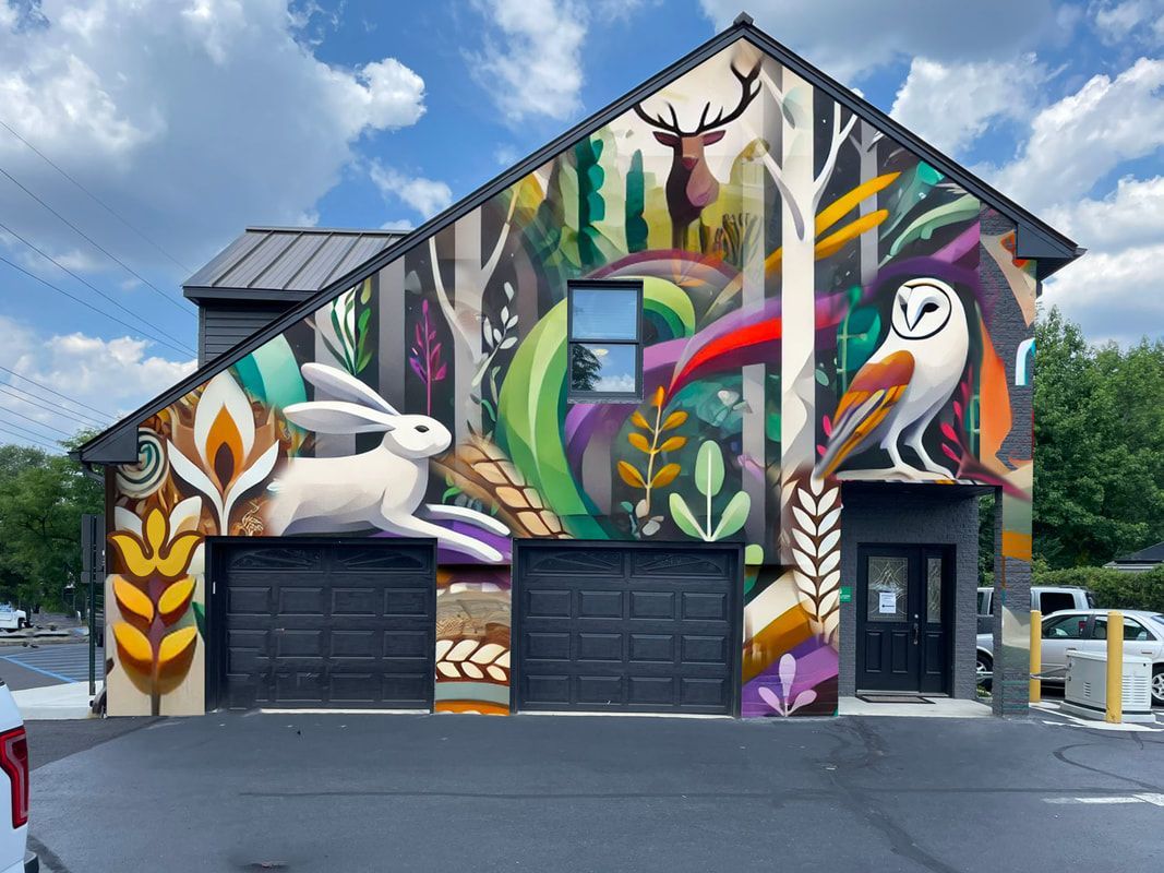 A vibrant mural on a two-story building featuring a large white rabbit, an owl, and a deer amidst stylized forest foliage.