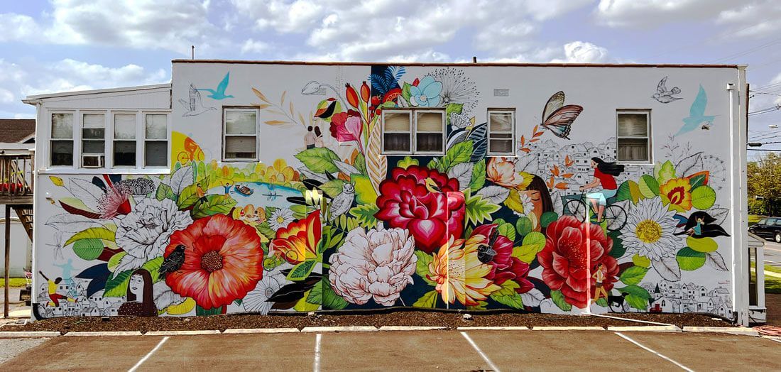 A vibrant floral mural painted across the side of a white building above a parking lot.