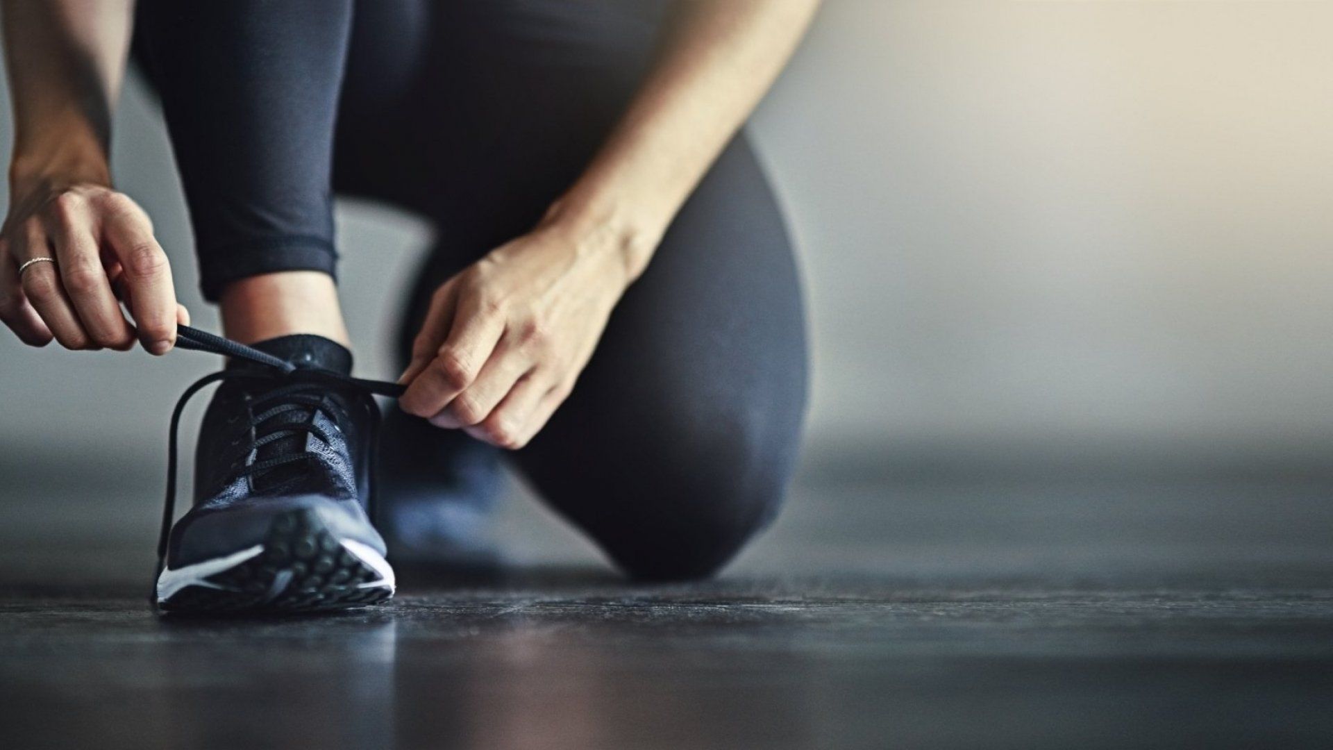 Person kneeling, tying running shoe laces.