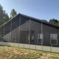 Dark gray house with white trim and a low concrete foundation in a grassy yard under a blue sky