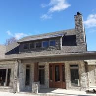 Stone house exterior with a dormer window, wooden front doors, and a tall chimney under a blue sky