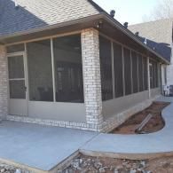 Screened porch attached to a brick house with a concrete walkway and landscaped bed