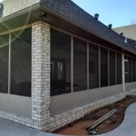 Screened porch on a brick house with a white brick corner and concrete walkway beside it