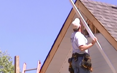Worker on a roof installing shingles on a house under a clear blue sky