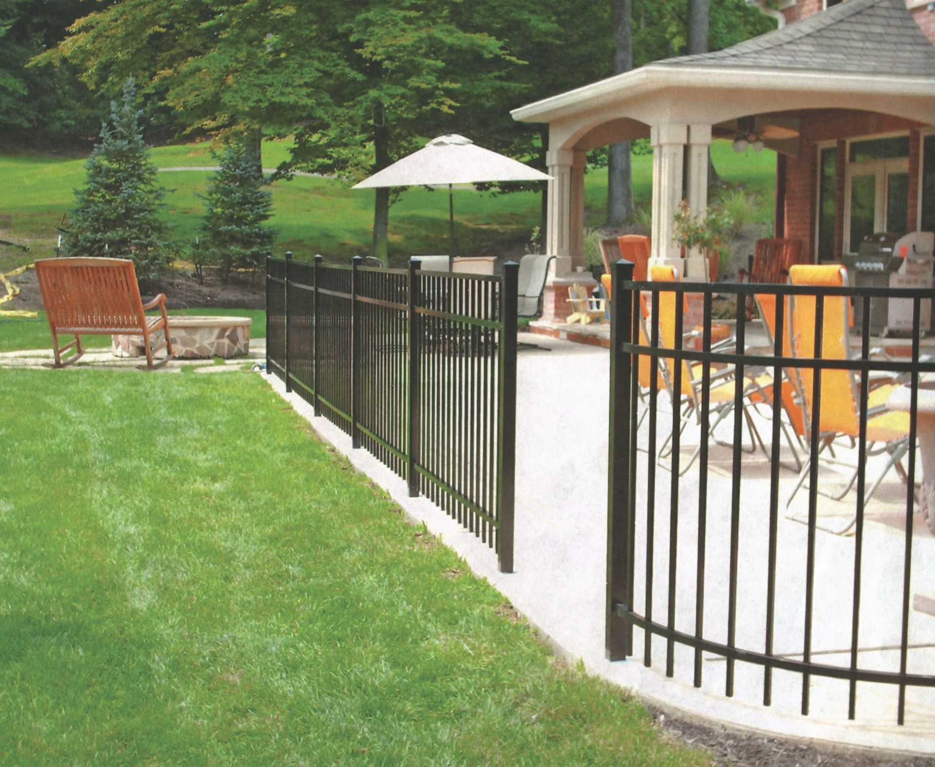 Black metal fence on a concrete patio next to a green lawn and a house with a patio.