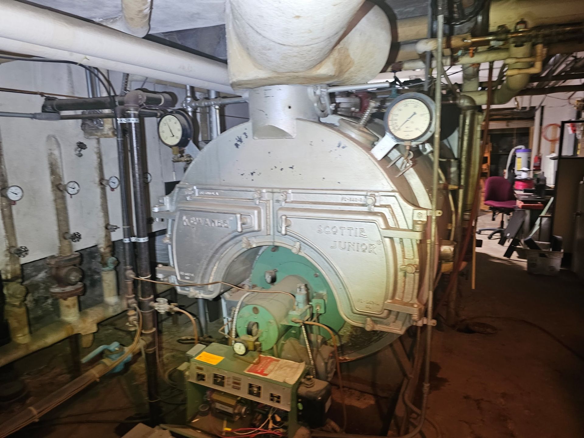 A large machine is sitting in a room with pipes and gauges.