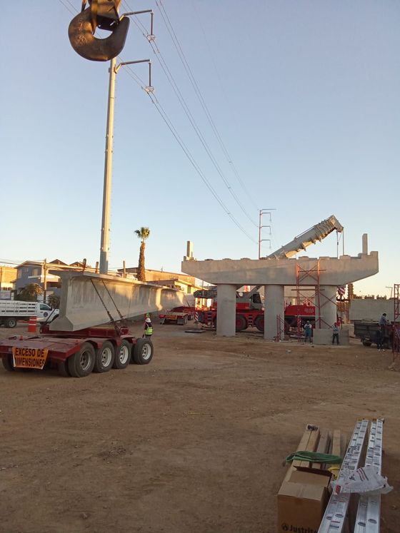 Sitio de construcción: Grúa levantando sección de puente de concreto cerca de líneas eléctricas y soportes.