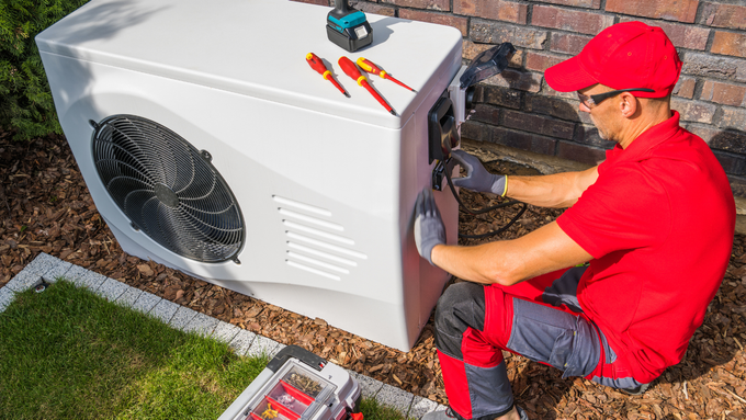 A man in a red shirt is working on a heat pump.