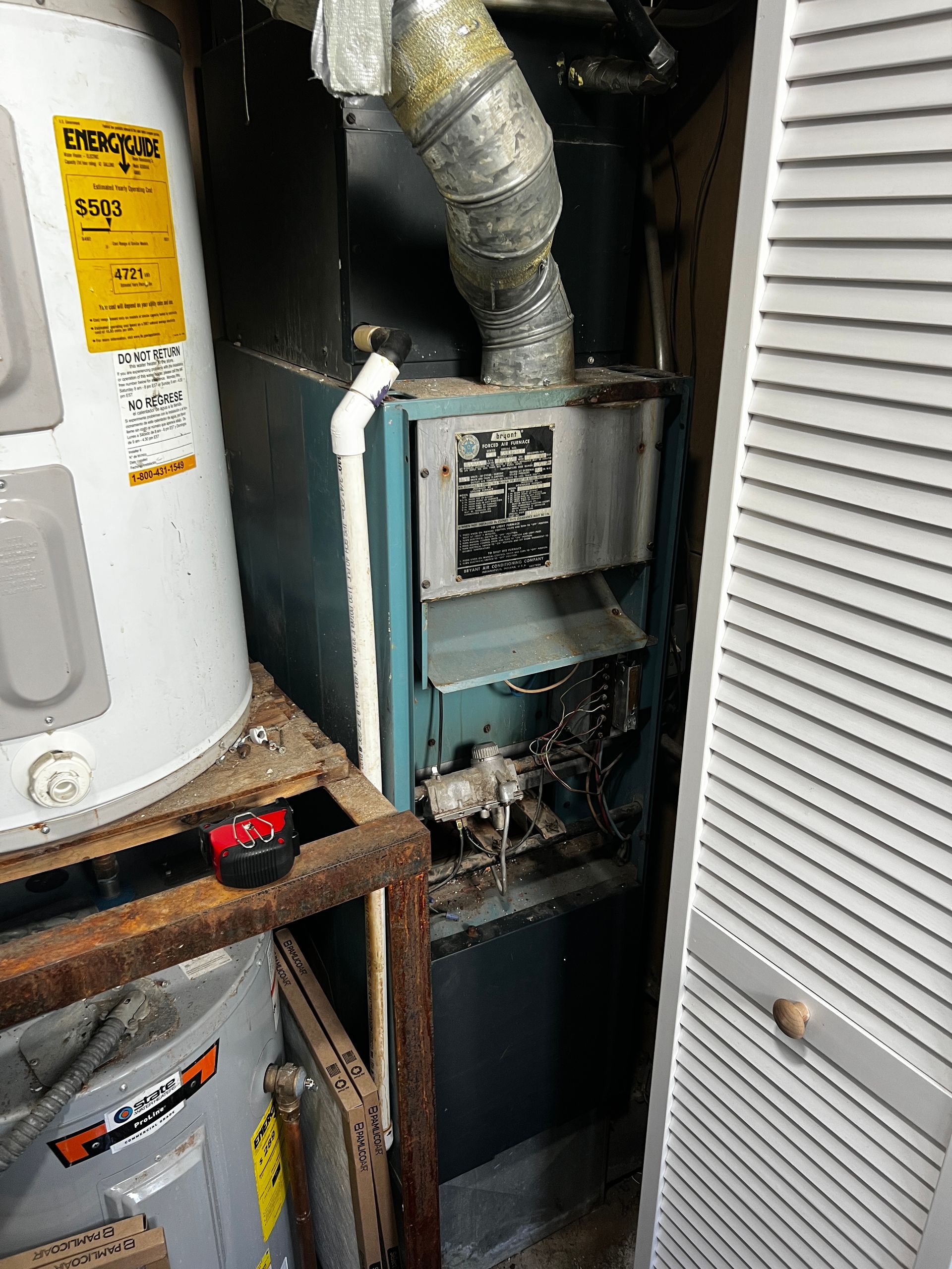 A water heater is sitting next to a furnace in a closet.
