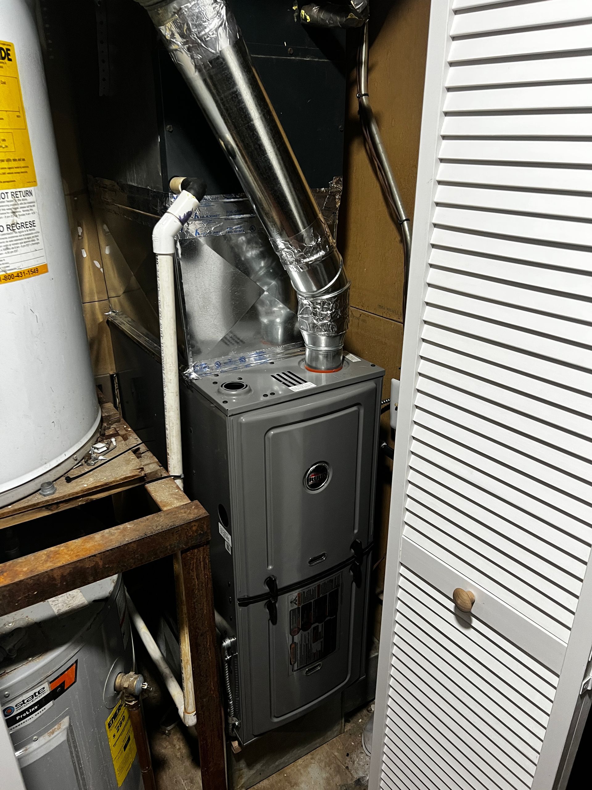 A furnace is sitting in a closet next to a water heater.