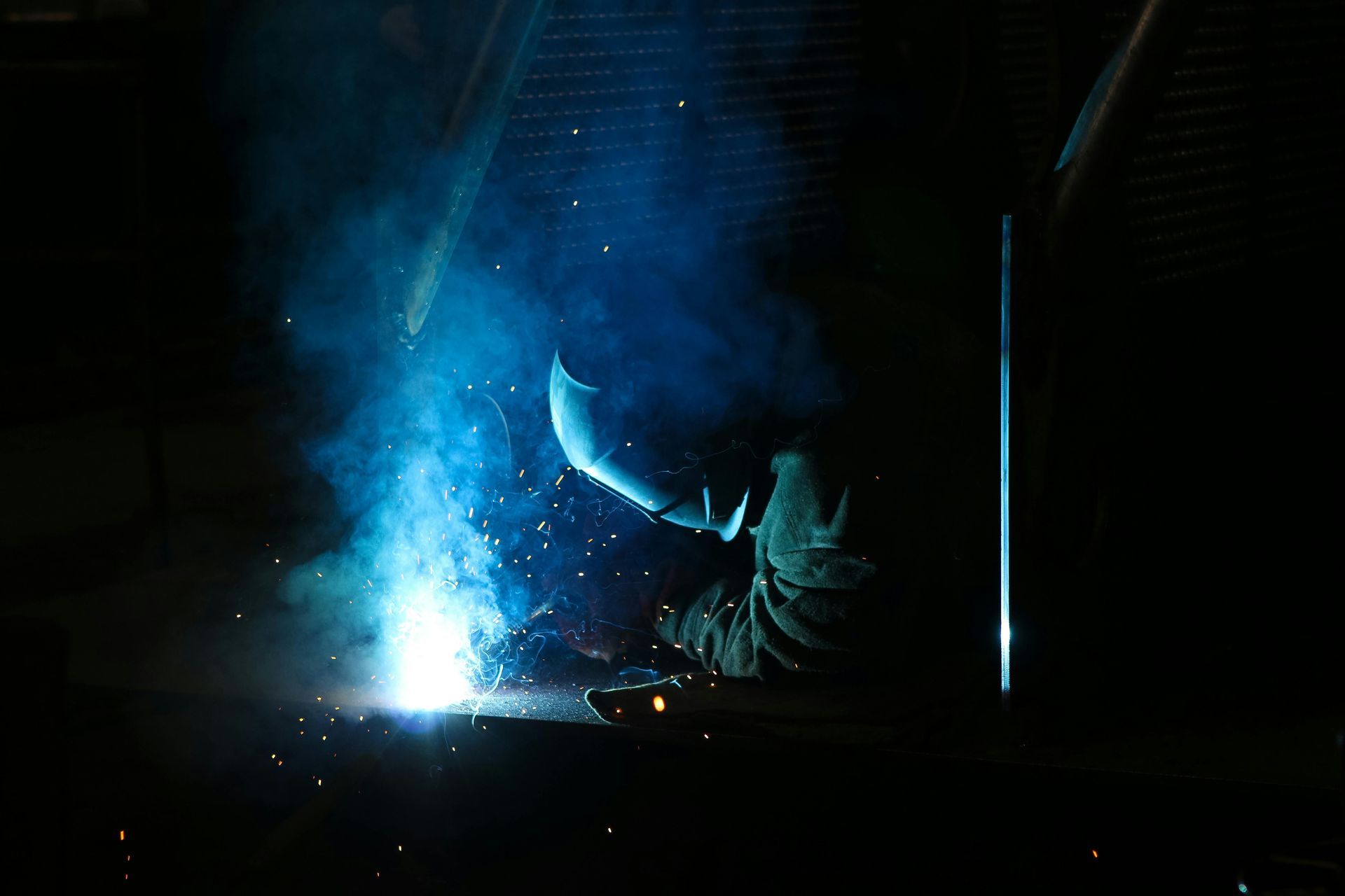 A man is welding a piece of metal in a dark room.